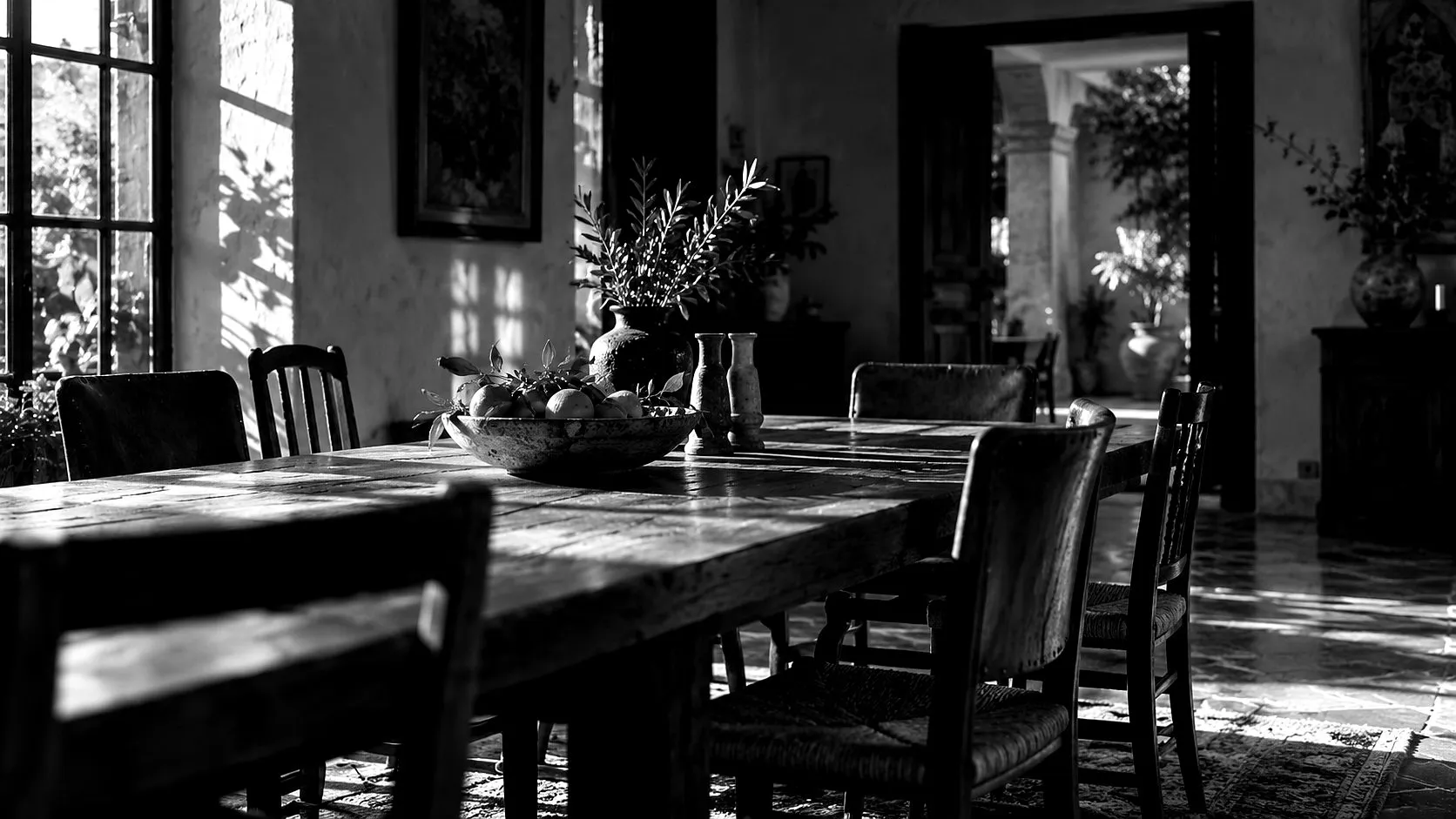Mesa larga de madera con sillas de distintos estilos en una casa familiar, con luz de tarde.